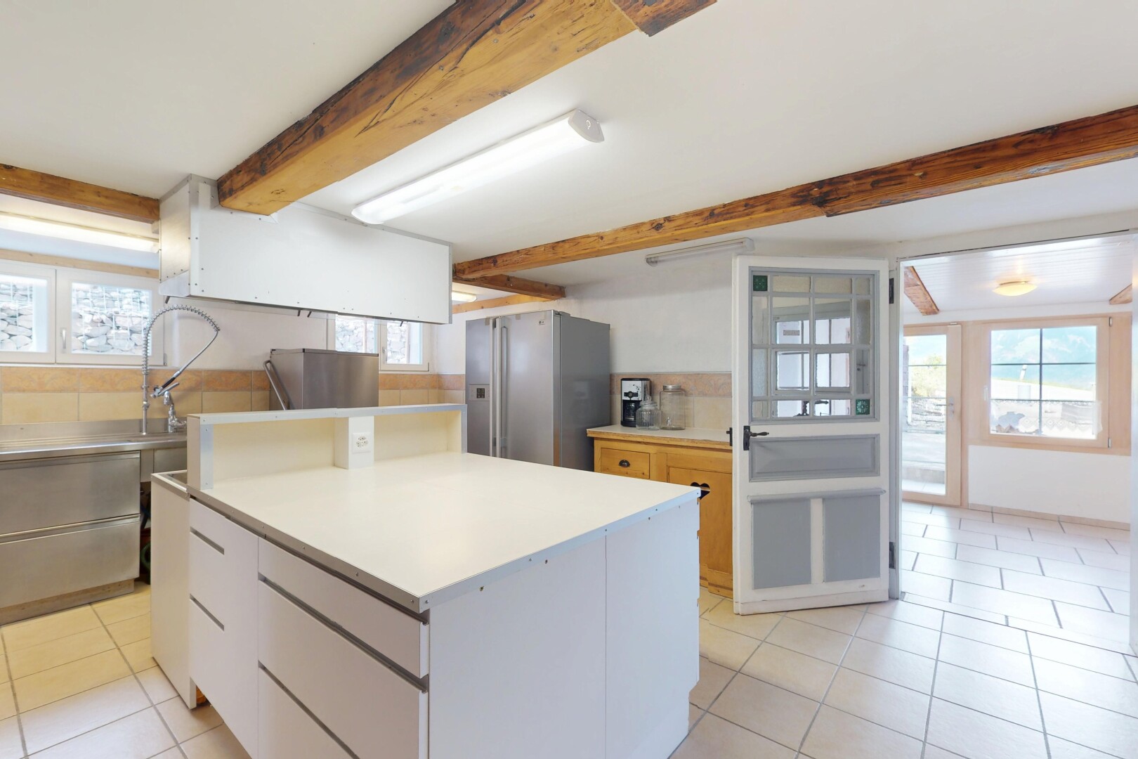 cuisine avec lumière naturelle, réfrigérateur, sol en carrelage, et plafond à poutres