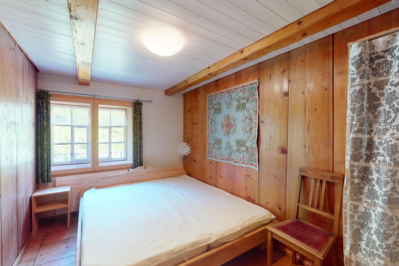 chambre avec mur en bois, lumière naturelle, et plafond à poutres