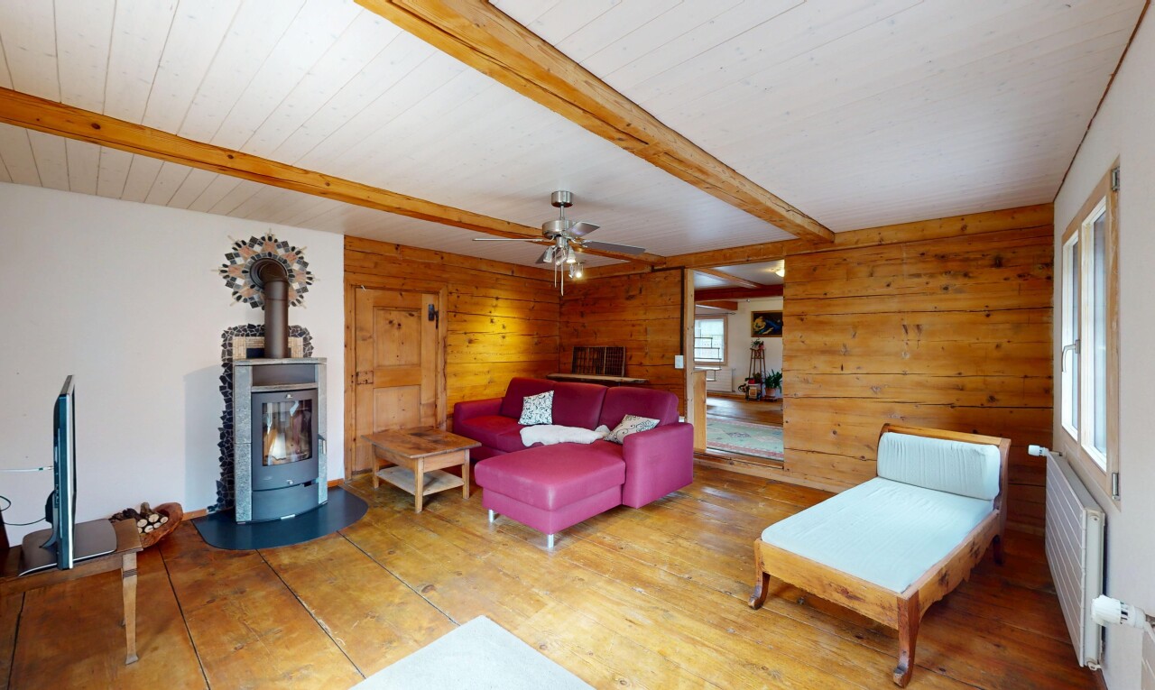 salon avec lumière naturelle, plafond à poutres, poêle à bois, et mur en bois