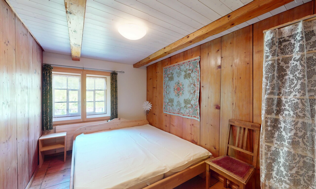 chambre avec mur en bois, lumière naturelle, et plafond à poutres