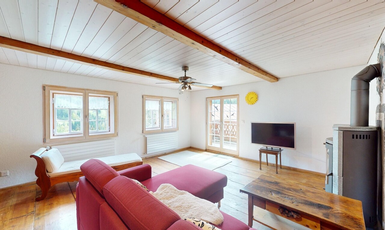 salon avec lumière naturelle, plafond à poutres, télévision, sol en finition bois, et cloison sèche
