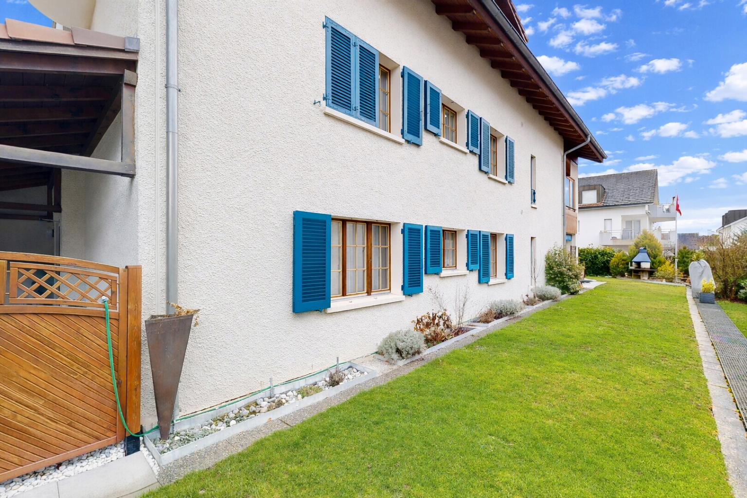 façade avec bardage en stuc, pelouse, property visible, et day time