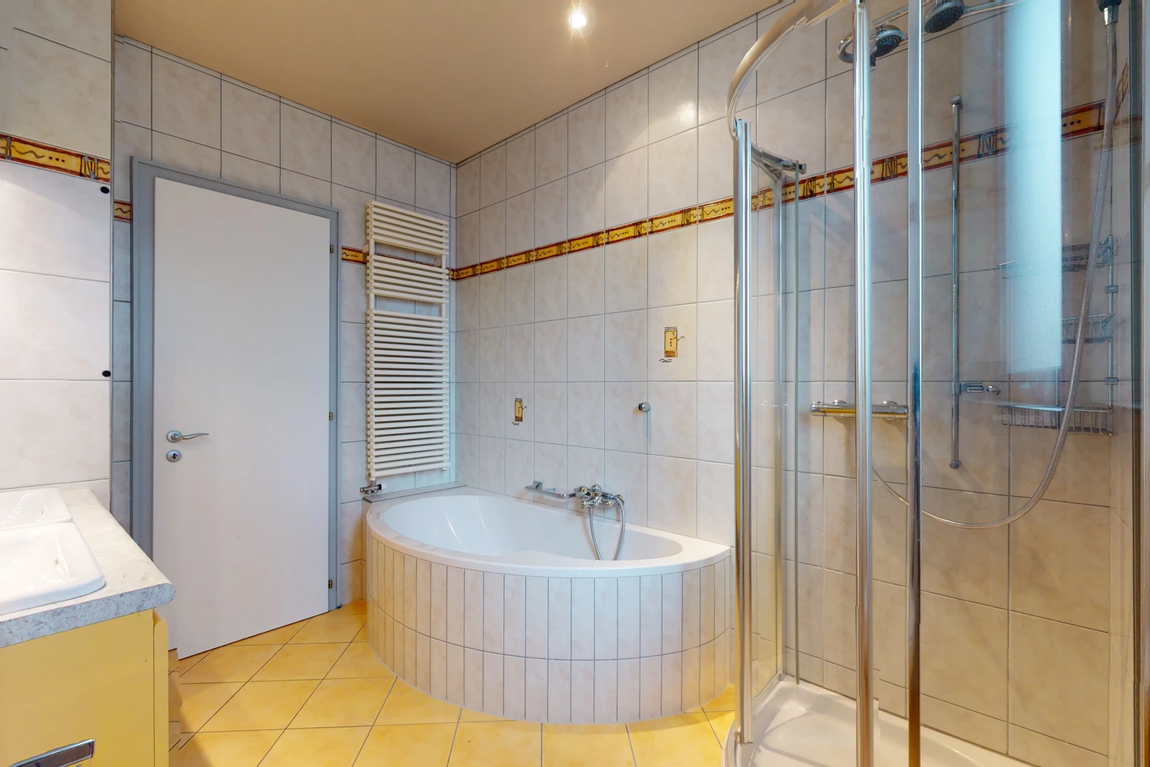 salle de bains avec carrelage, radiateur, vasque, porte de douche, meuble-lavabo, douche, et baignoire
