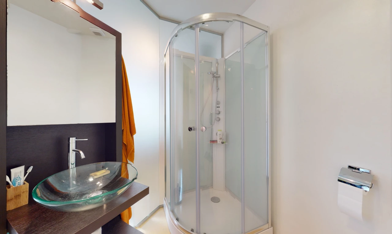 salle de bains avec vasque, porte de douche, miroir, meuble-lavabo, et douche