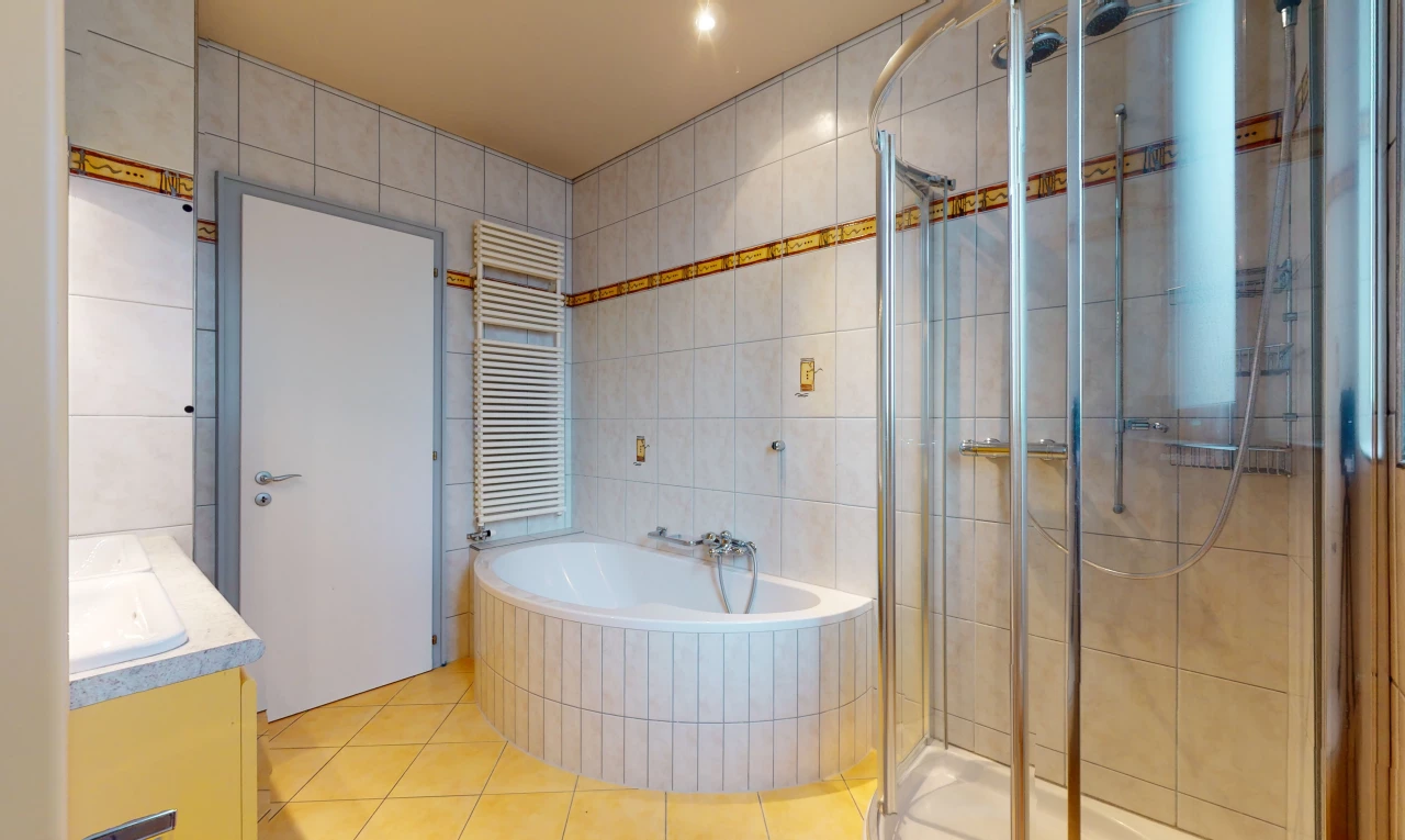 salle de bains avec carrelage, radiateur, vasque, porte de douche, meuble-lavabo, douche, et baignoire