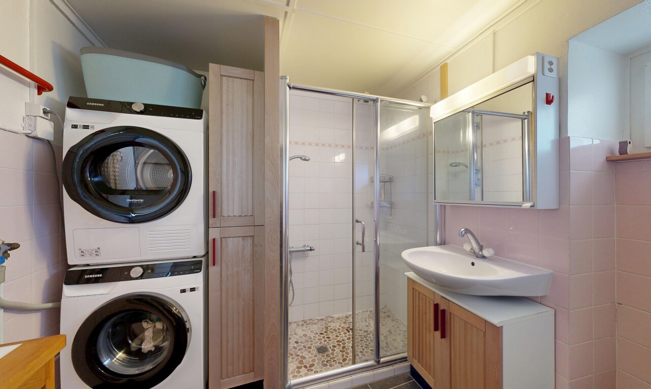 salle de bains avec miroir, lavabo (ou coiffeuse selon le contexte), salle de bain complète, douche, et lave-linge et sèche-linge superposés