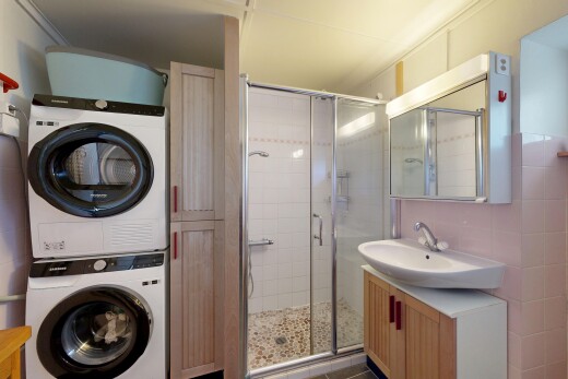 salle de bains avec miroir, lavabo (ou coiffeuse selon le contexte), salle de bain complète, douche, et lave-linge et sèche-linge superposés