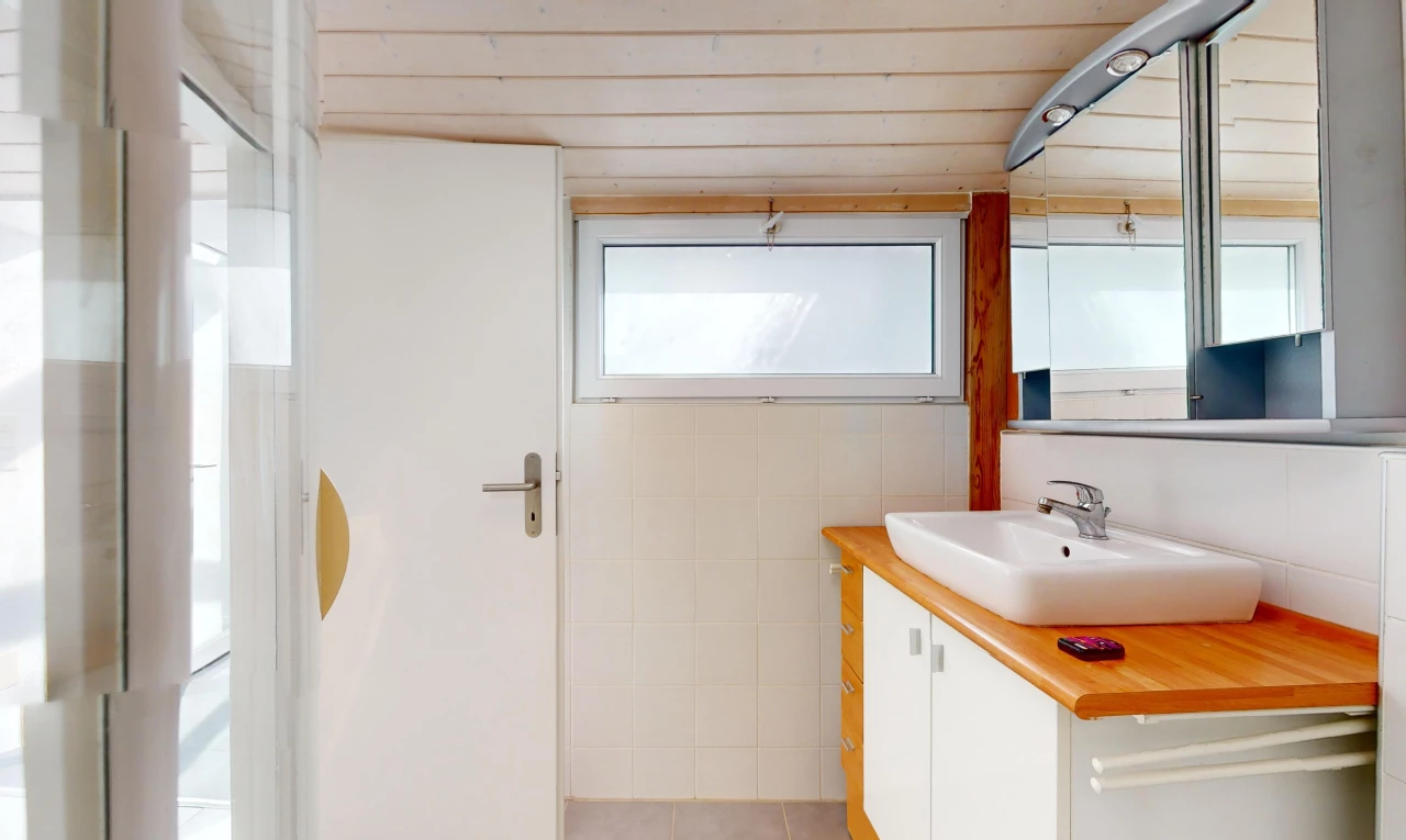 salle de bain avec meuble-lavabo, miroir, lumière naturelle, et vasque
