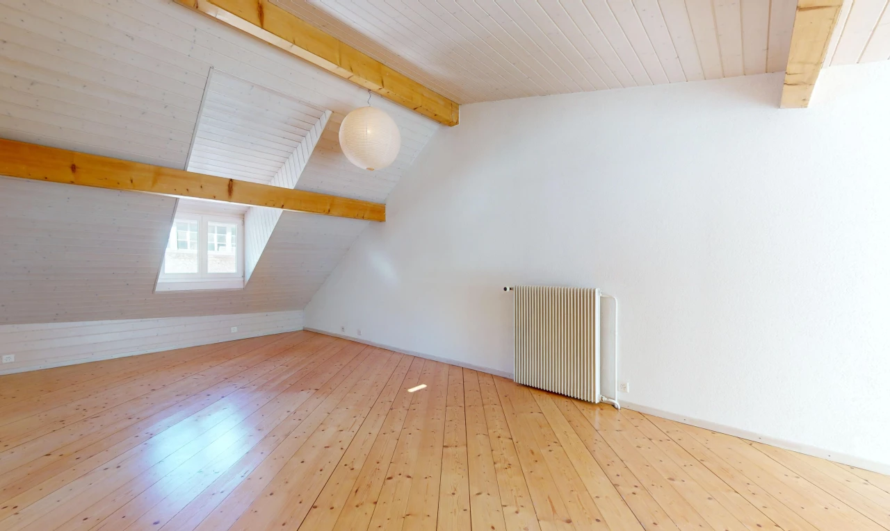 pièce vide avec plancher de bois, lumière naturelle, poutres apparentes, radiateur, et plafond voûté