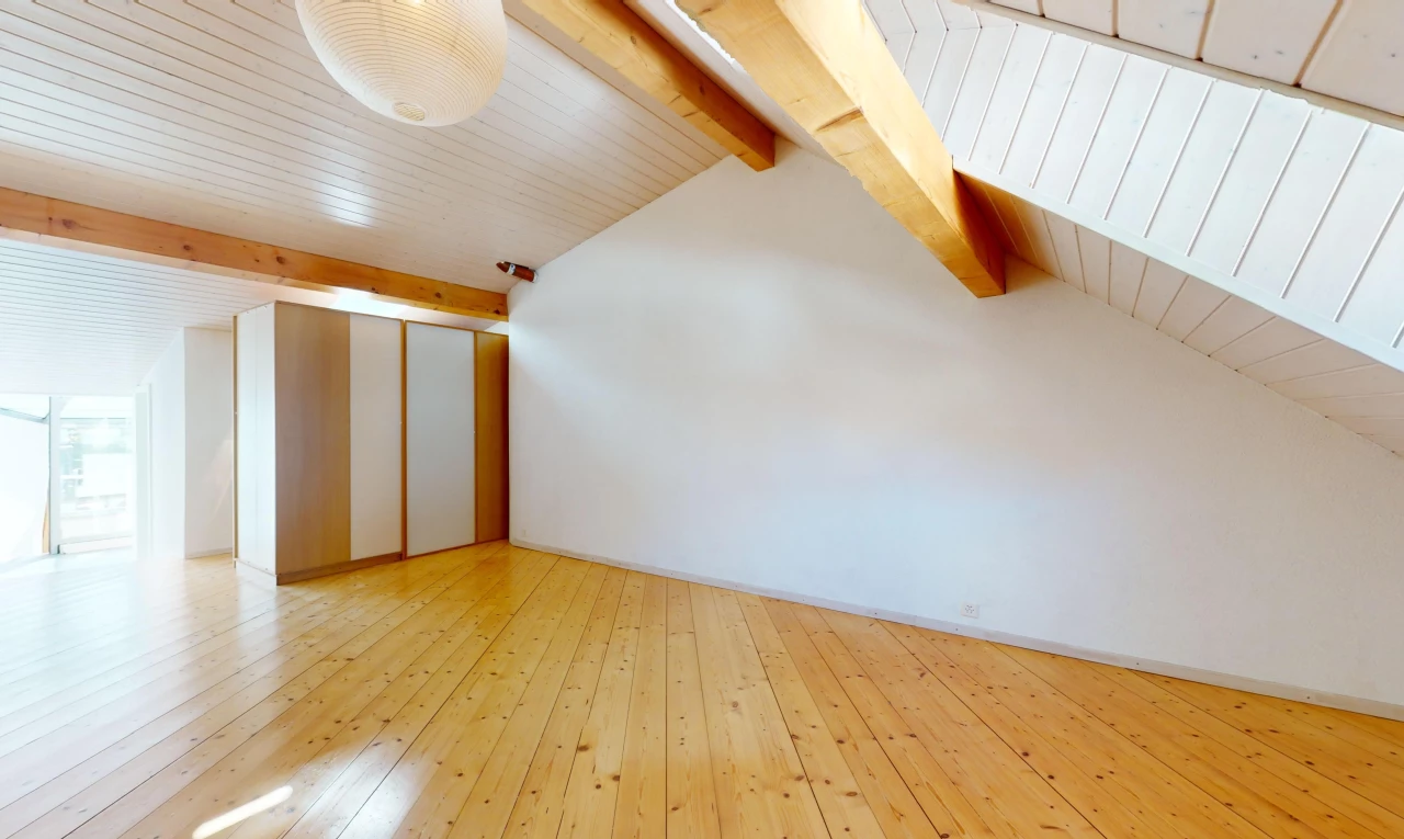 pièce vide avec poutres apparentes, plafond voûté, et plancher de bois