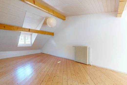 pièce vide avec plancher de bois, lumière naturelle, poutres apparentes, radiateur, et plafond voûté