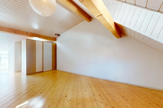 pièce vide avec poutres apparentes, plafond voûté, et plancher de bois