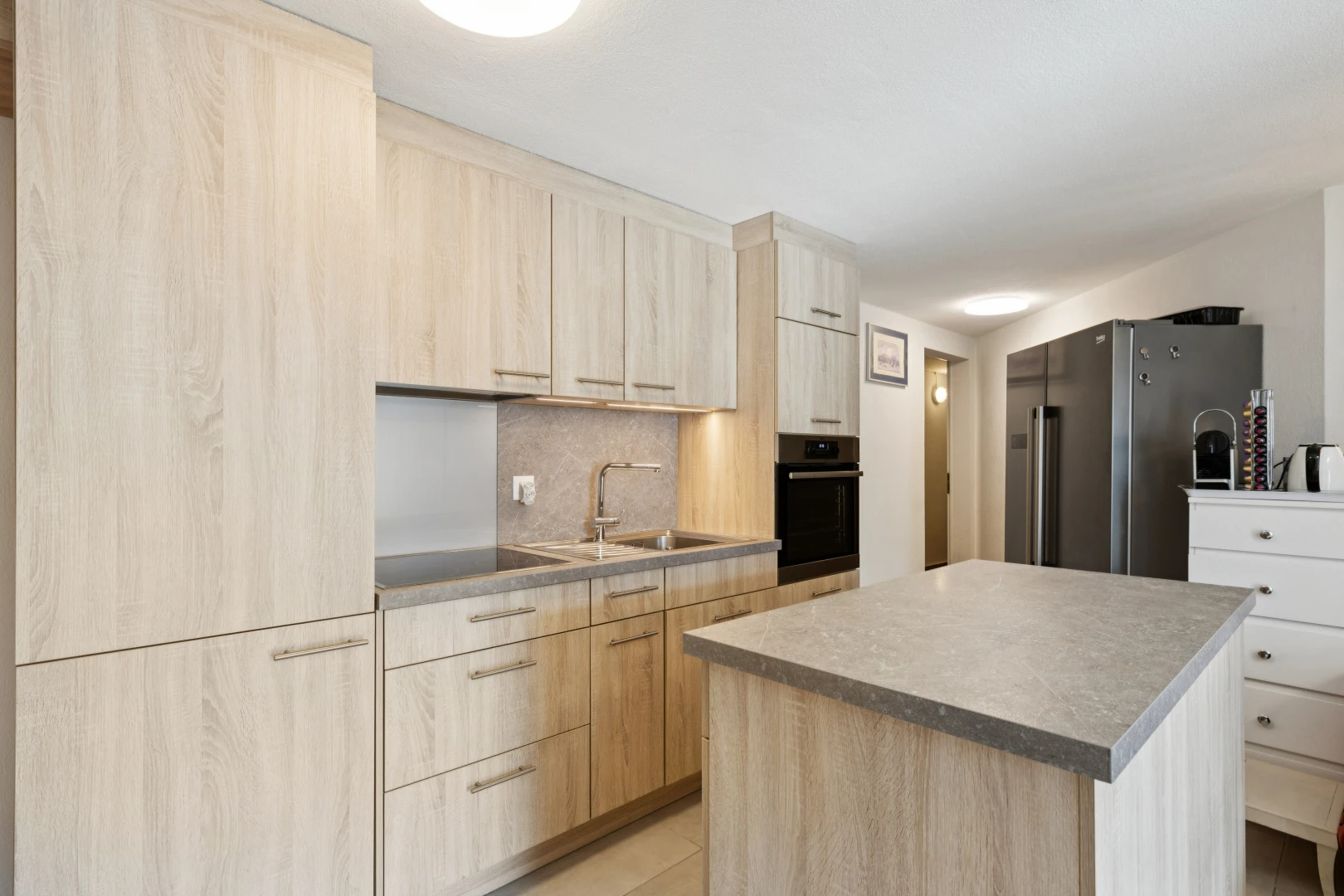 cuisine avec armoires marron clair, light brown cabinets, réfrigérateur, four, et îlot de cuisine
