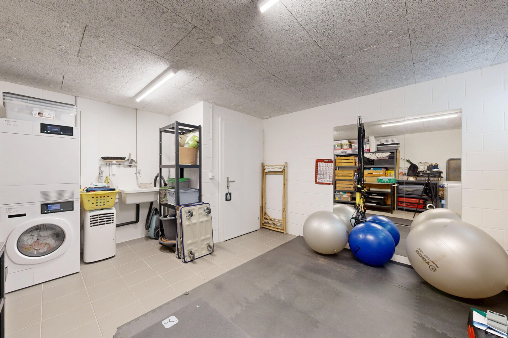 gym avec inside property, lave-linge et sèche-linge superposés, mur en blocs de béton, concrete block wall, et light floor