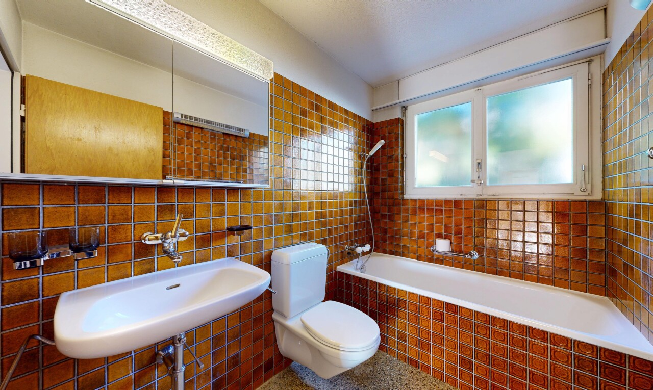 salle de bains avec toilette, miroir, évier, mur en carrelage, et tile wall