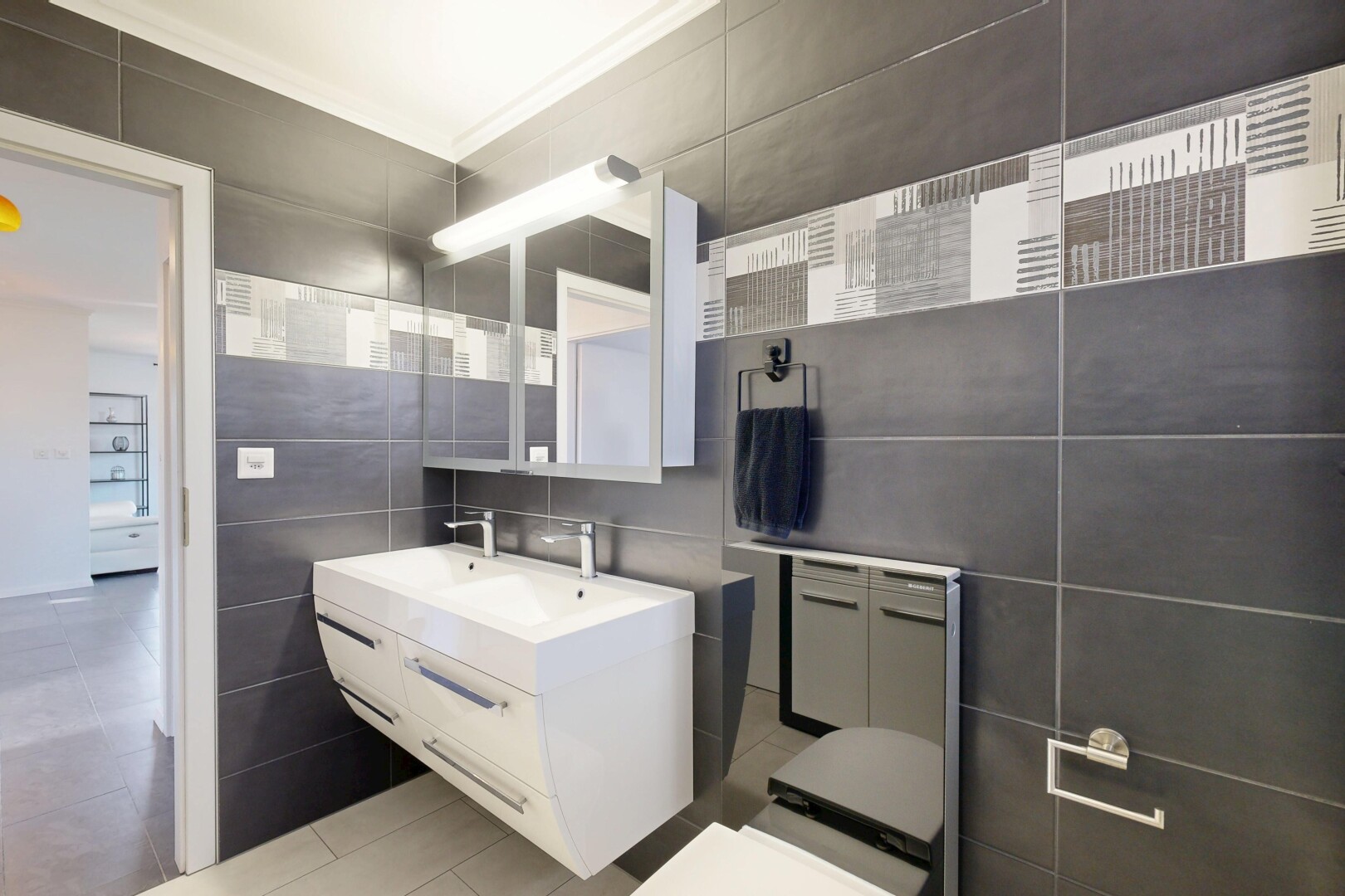 salle de bains avec mur en carrelage, tile wall, miroir, lavabo (ou coiffeuse selon le contexte), et light floor