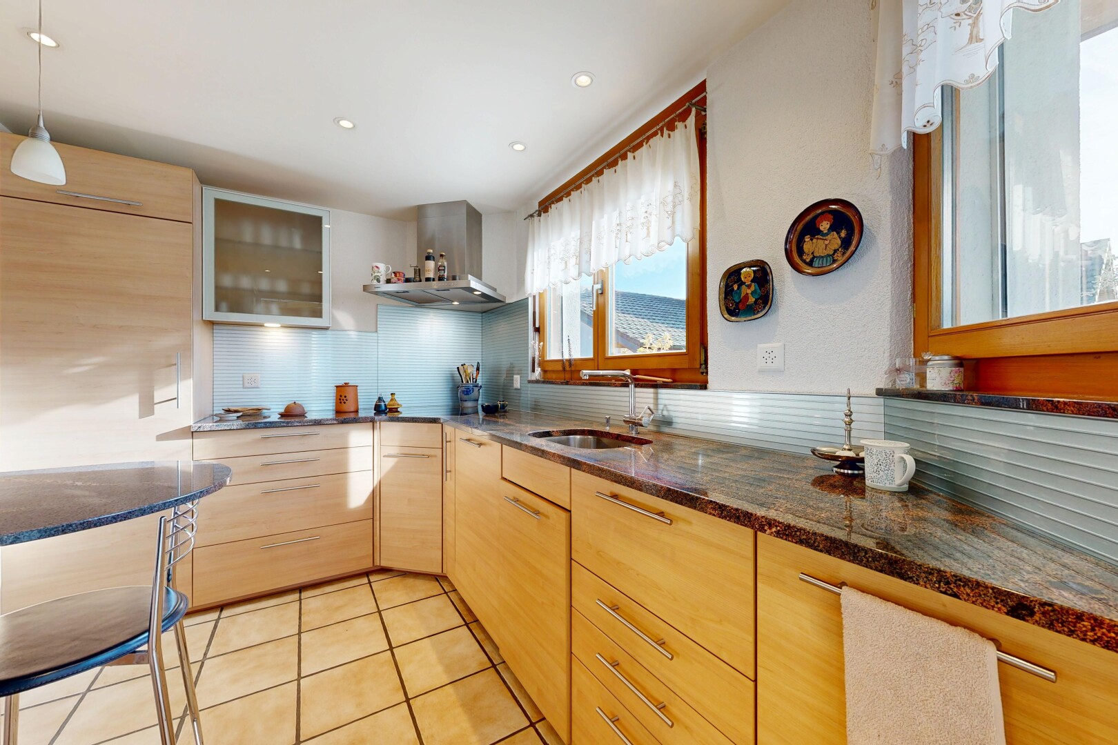 cuisine avec armoires marron clair, light brown cabinets, armoires avec insert en verre, glass insert cabinets, et dark countertops