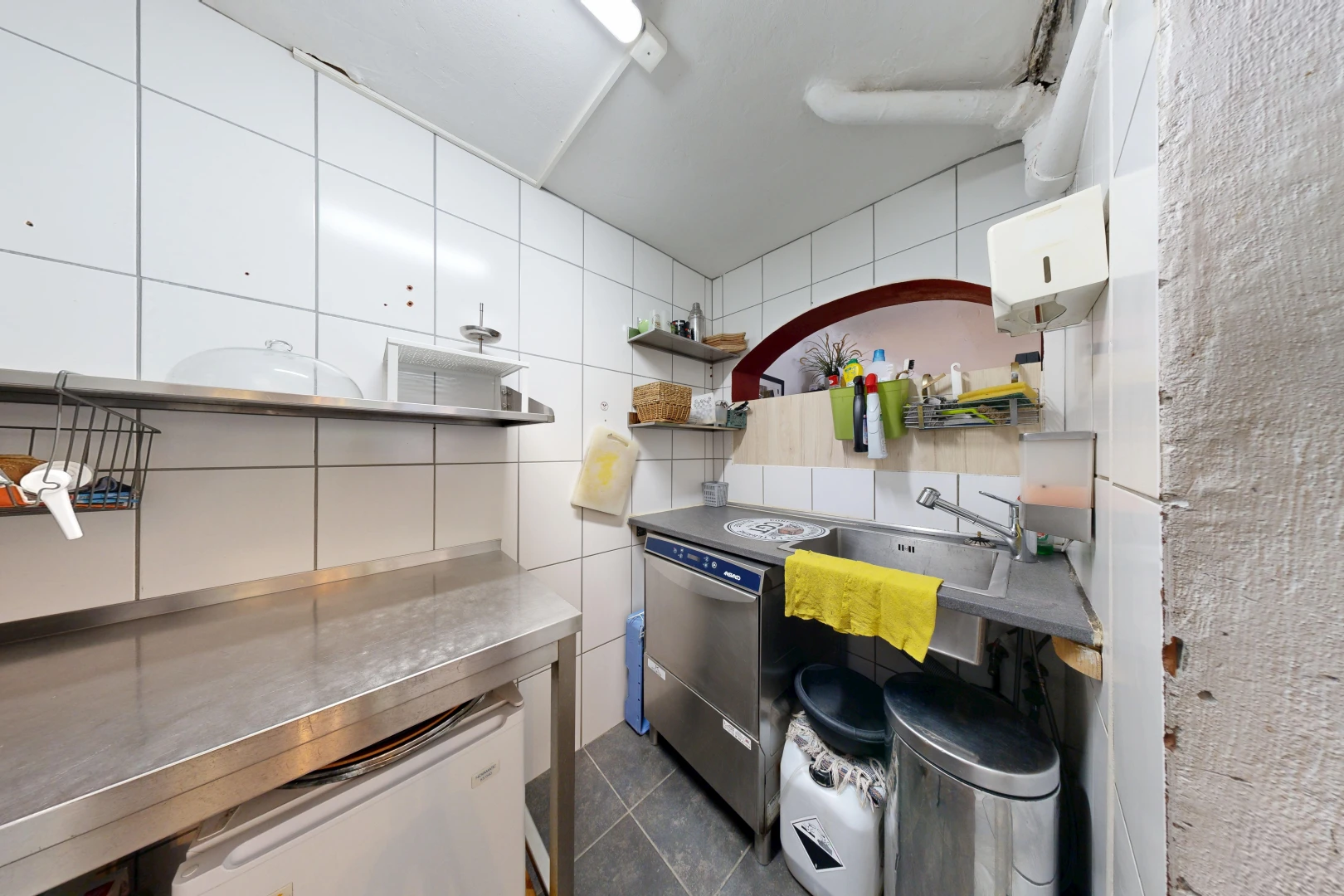 cuisine avec plans de travail en acier inoxydable, stainless steel countertops, mur en carrelage, tile wall, et dark floor