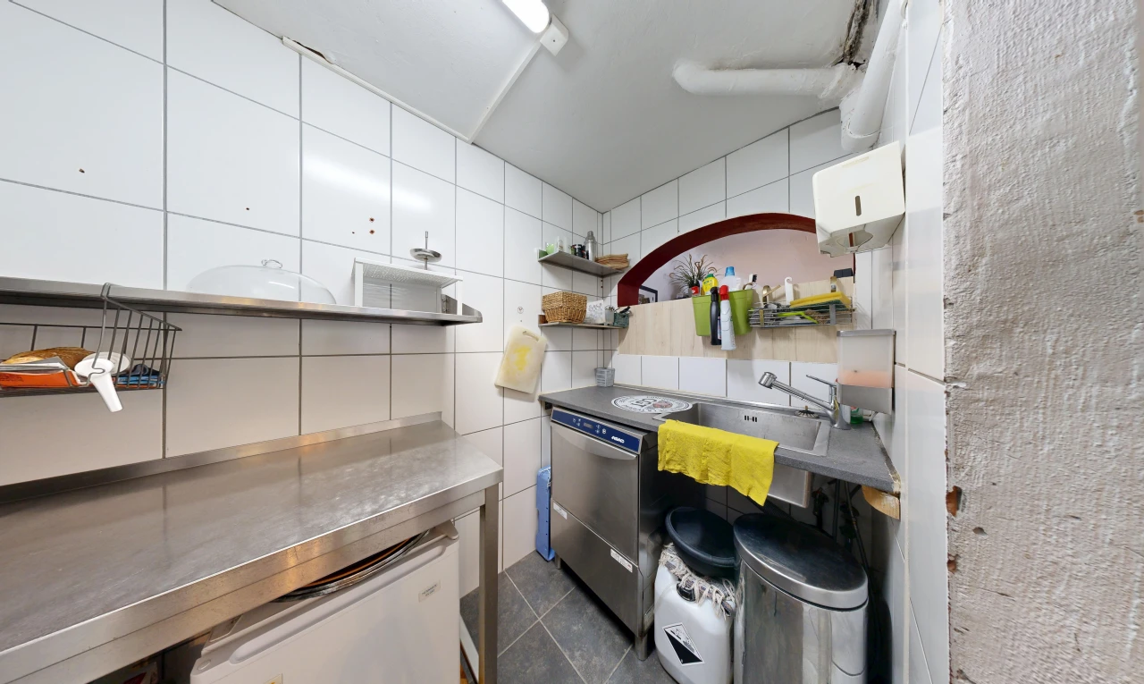 cuisine avec plans de travail en acier inoxydable, stainless steel countertops, mur en carrelage, tile wall, et dark floor