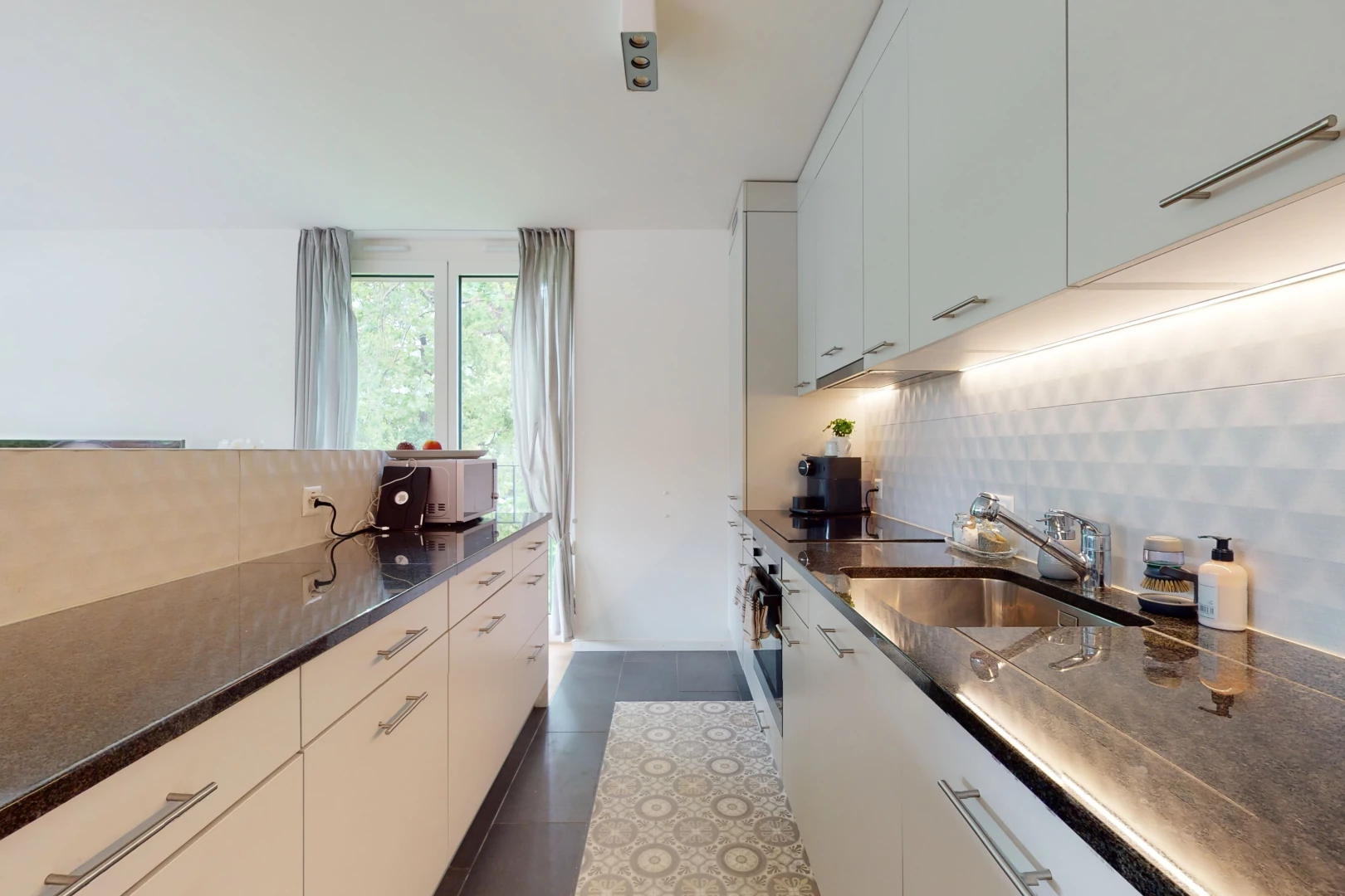 cuisine avec lumière naturelle, cuisinière électrique, meubles blancs, et plan de travail foncé
