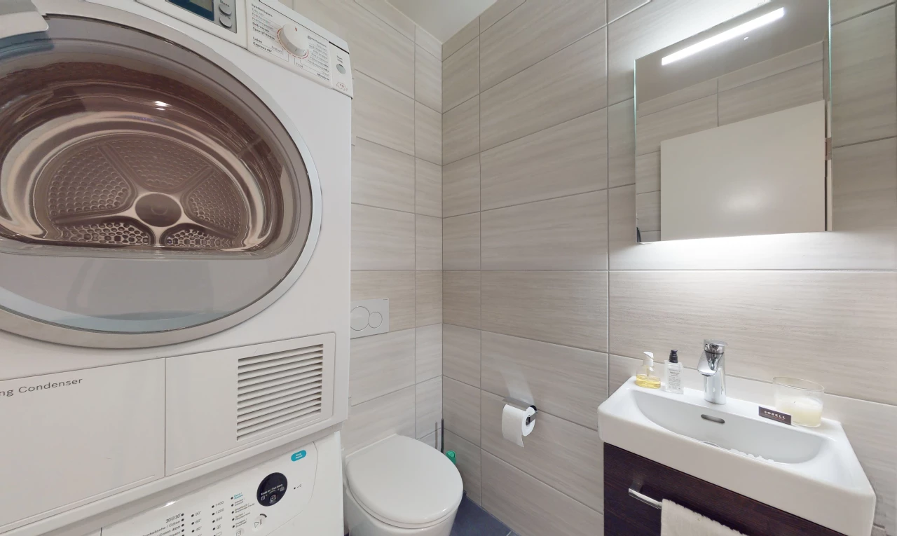 salle de bains avec machine à laver / sèche-linge, vasque, toilettes, miroir, et meuble-lavabo