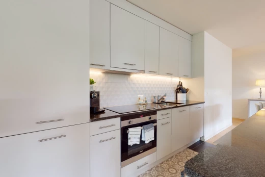 cuisine avec four, cuisinière électrique, meubles blancs, et plan de travail foncé