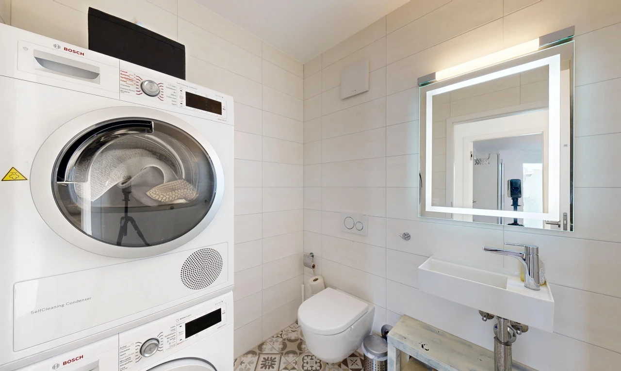 salle de bains avec miroir, lave-linge et sèche-linge superposés, mur en carrelage, tile wall, et toilette
