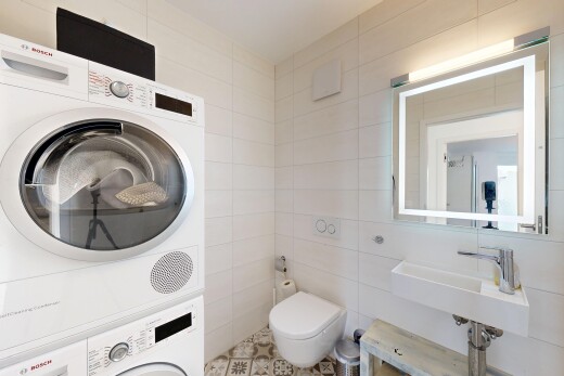salle de bains avec miroir, lave-linge et sèche-linge superposés, mur en carrelage, tile wall, et toilette