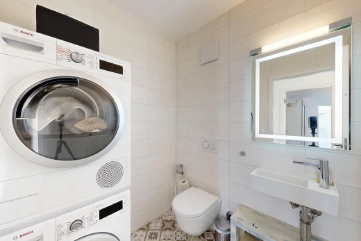 salle de bains avec miroir, lave-linge et sèche-linge superposés, mur en carrelage, tile wall, et toilette
