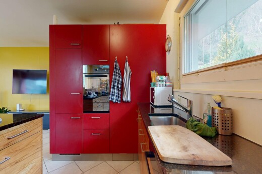 cuisine avec armoires rouges, red cabinets, dark countertops, télévision, et four