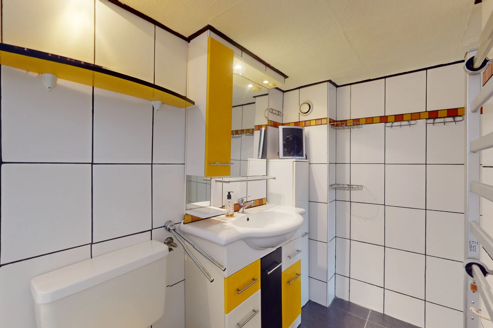 salle de bain avec mur carrelé, vasque, toilettes, et miroir
