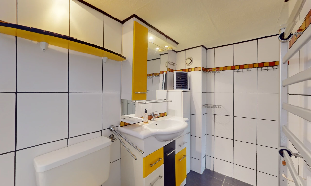 salle de bain avec mur carrelé, vasque, toilettes, et miroir