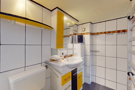 salle de bain avec mur carrelé, vasque, toilettes, et miroir