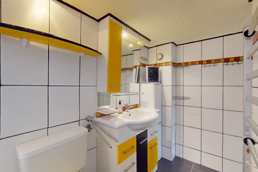 salle de bain avec mur carrelé, vasque, toilettes, et miroir
