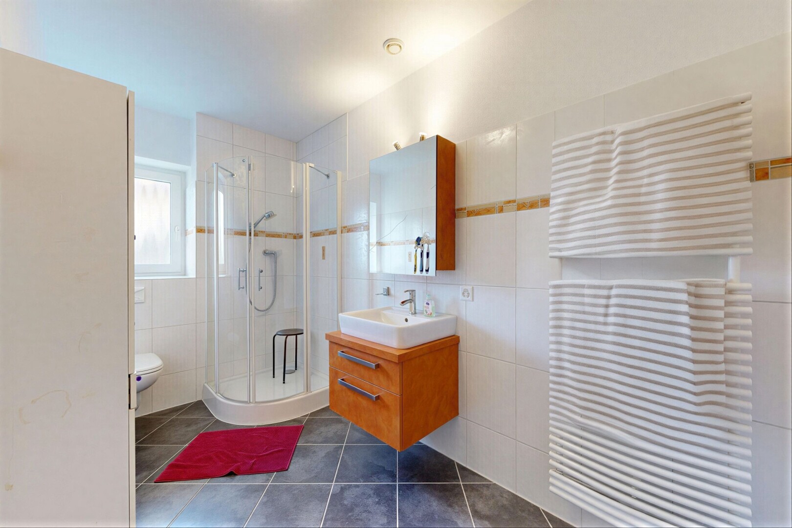 salle de bains avec radiateur, lavabo (ou coiffeuse selon le contexte), douche, dark floor, et mur en carrelage