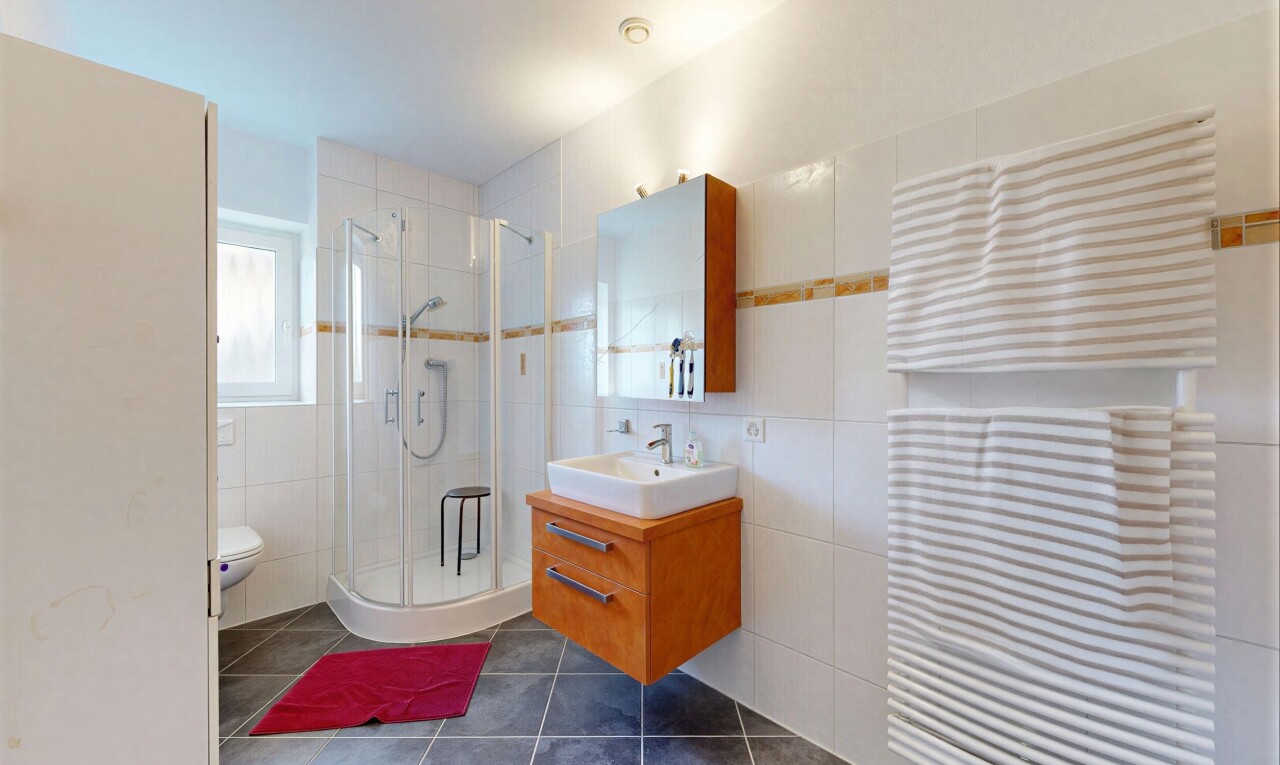 salle de bains avec radiateur, lavabo (ou coiffeuse selon le contexte), douche, dark floor, et mur en carrelage