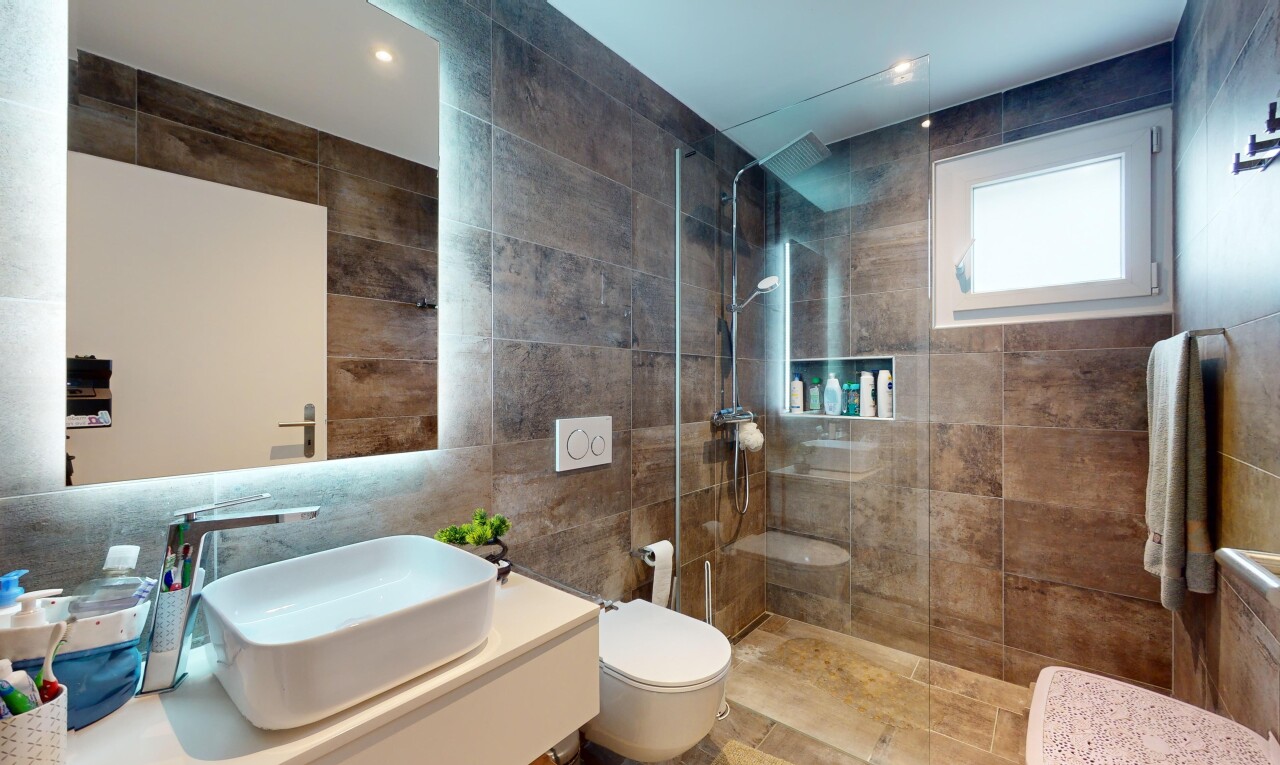 salle de bains avec vasque, lumière naturelle, miroir, douche, et mur carrelé
