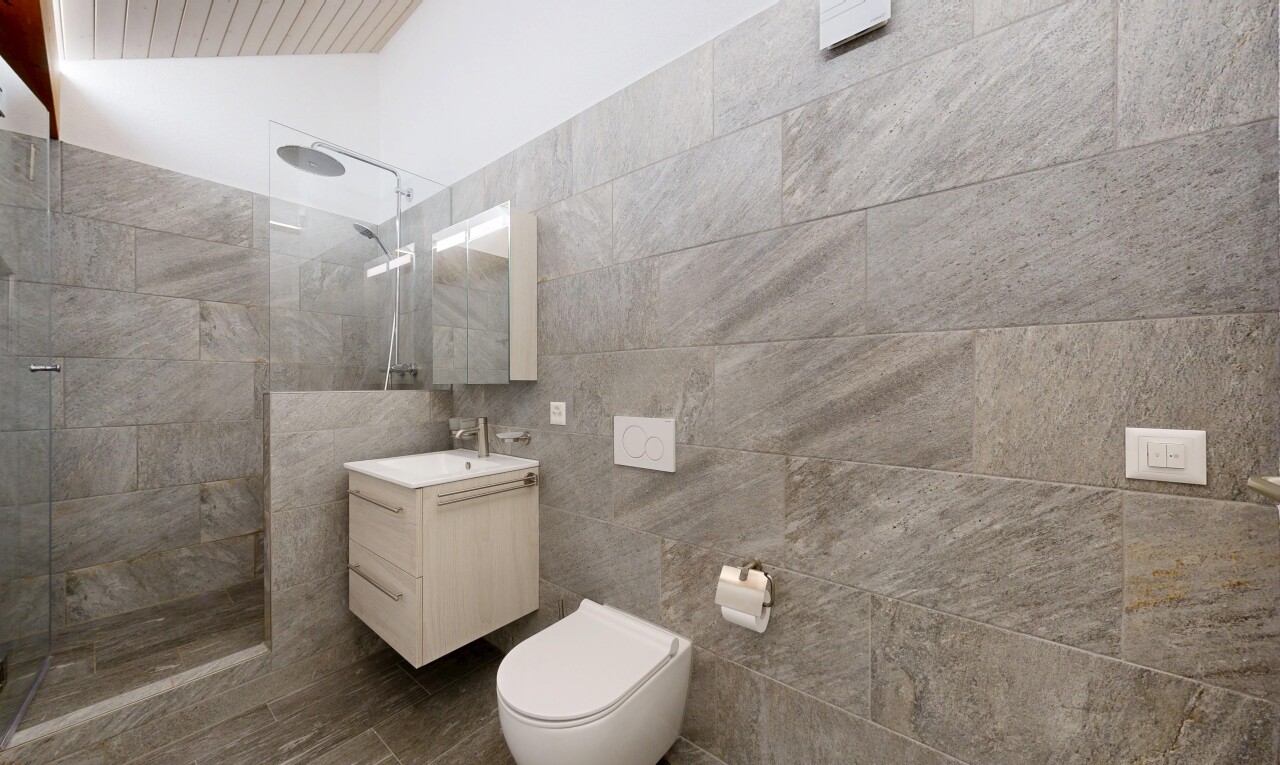 bathroom with walk in shower, vanity, tile walls, and lofted ceiling
