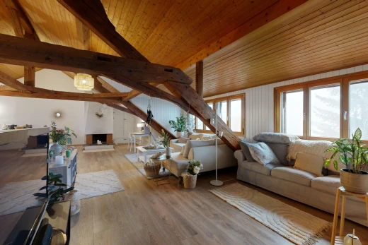 salon avec cheminée, plancher de bois, poutres apparentes, lumière naturelle, et plafond voûté