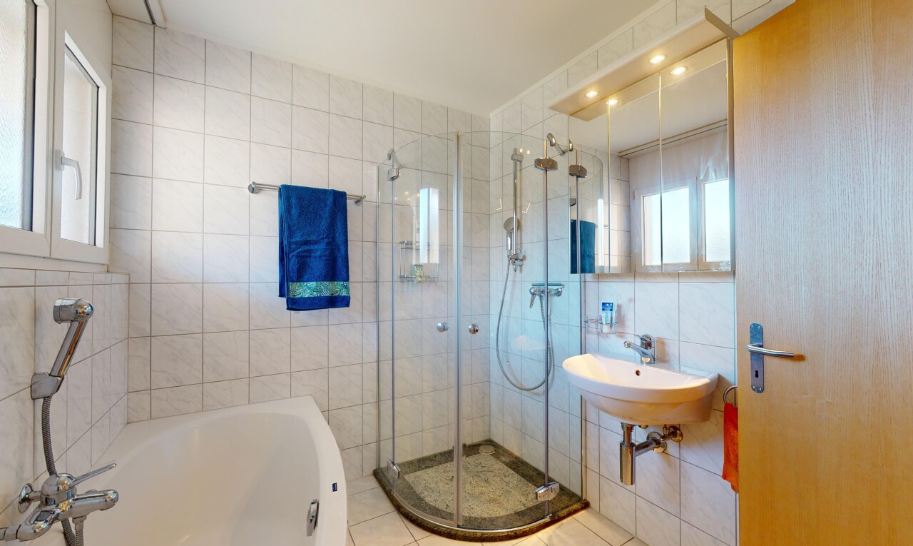 salle de bains avec douche, mur carrelé, miroir, et lumière naturelle