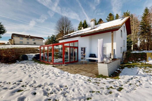 snow covered house featuring a patio, a sunroom, stucco siding, and a chimney