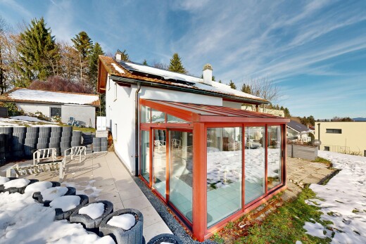 snow covered house with solar panels, a sunroom, a chimney, and a fenced backyard
