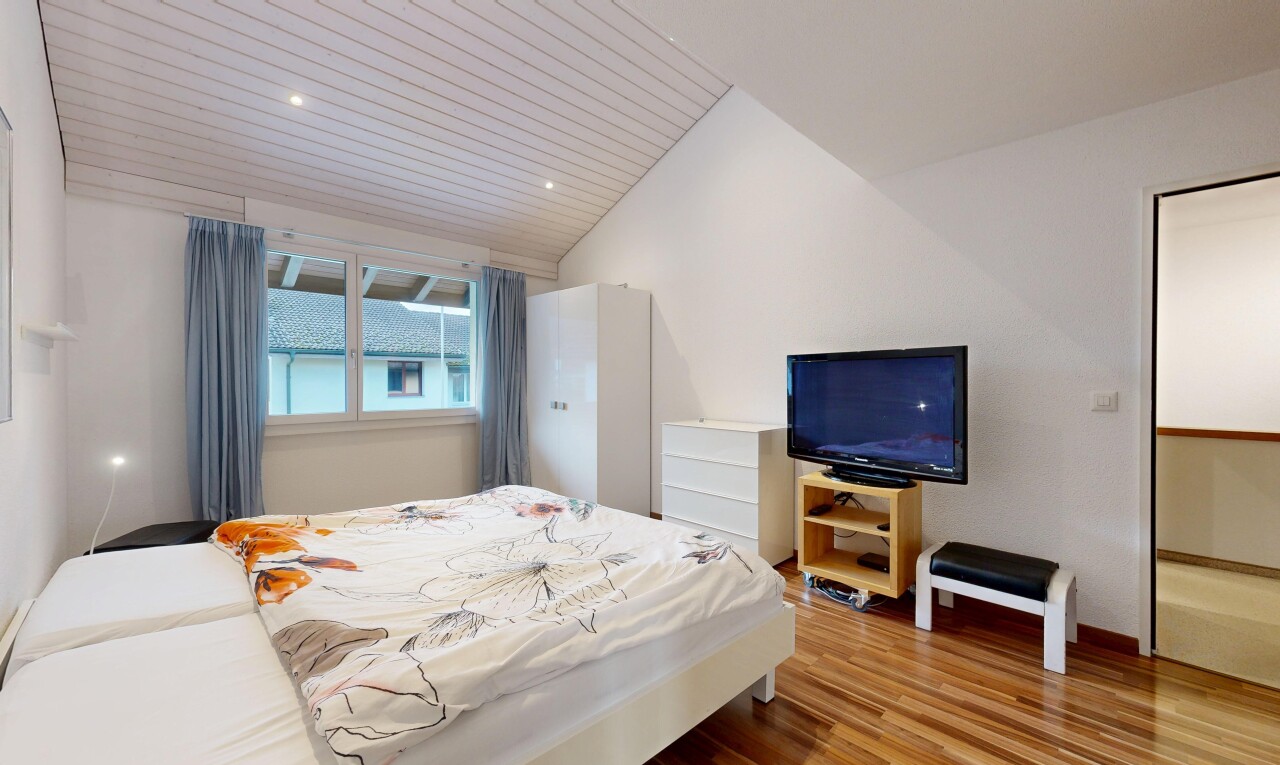 zimmer / schlafzimmer mit fernseher, vaulted ceiling, dachschräge, wood finish floor, und holzfußboden