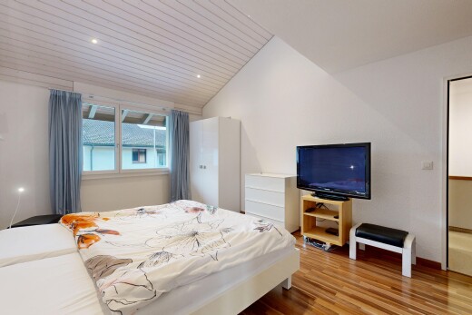zimmer / schlafzimmer mit fernseher, vaulted ceiling, dachschräge, wood finish floor, und holzfußboden