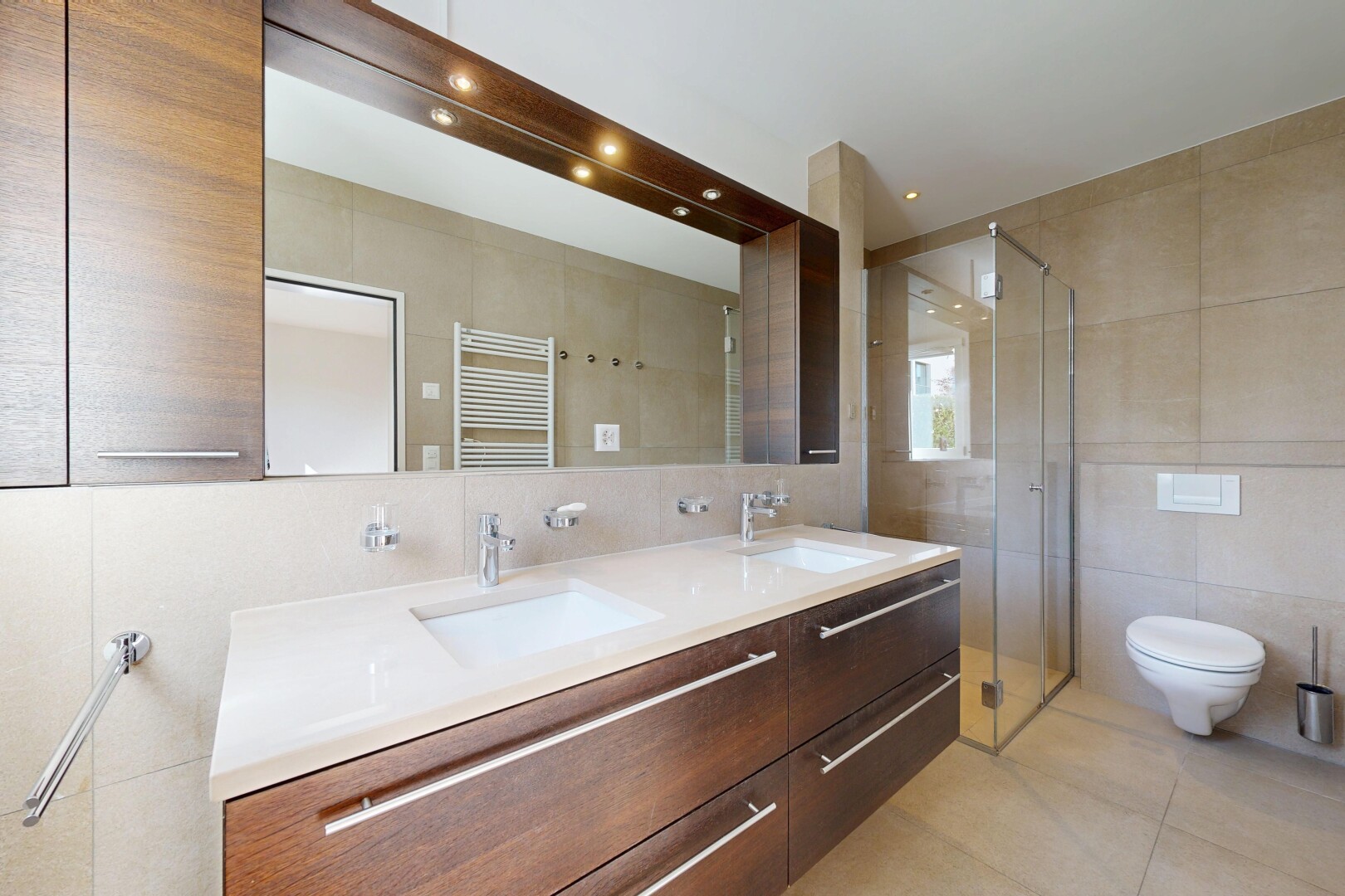 bathroom with tile walls, a stall shower, double vanity, a towel warmer, and radiator