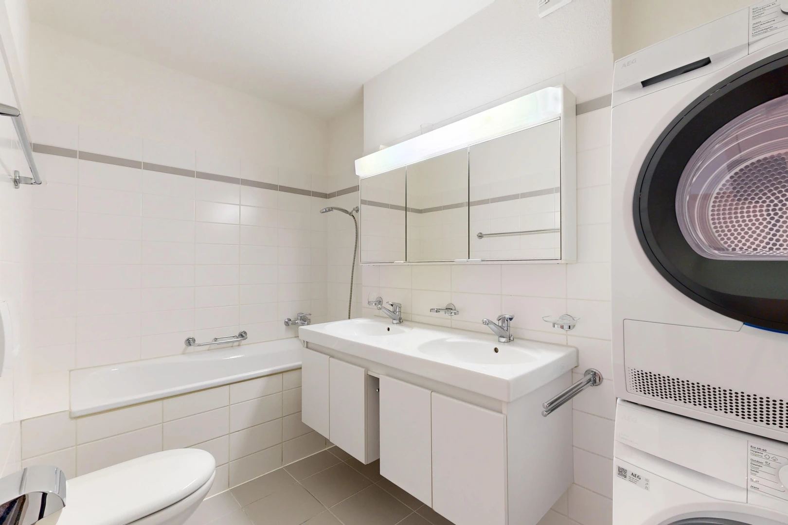 salle de bains avec miroir, salle de bain complète, double vasque, toilette, et lave-linge et sèche-linge superposés