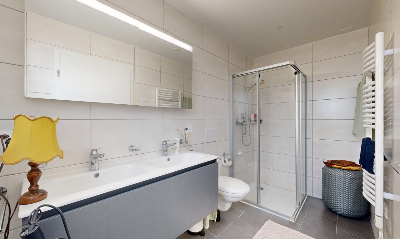 bathroom with tile walls, a stall shower, a towel warming rack, double vanity, and tile patterned flooring