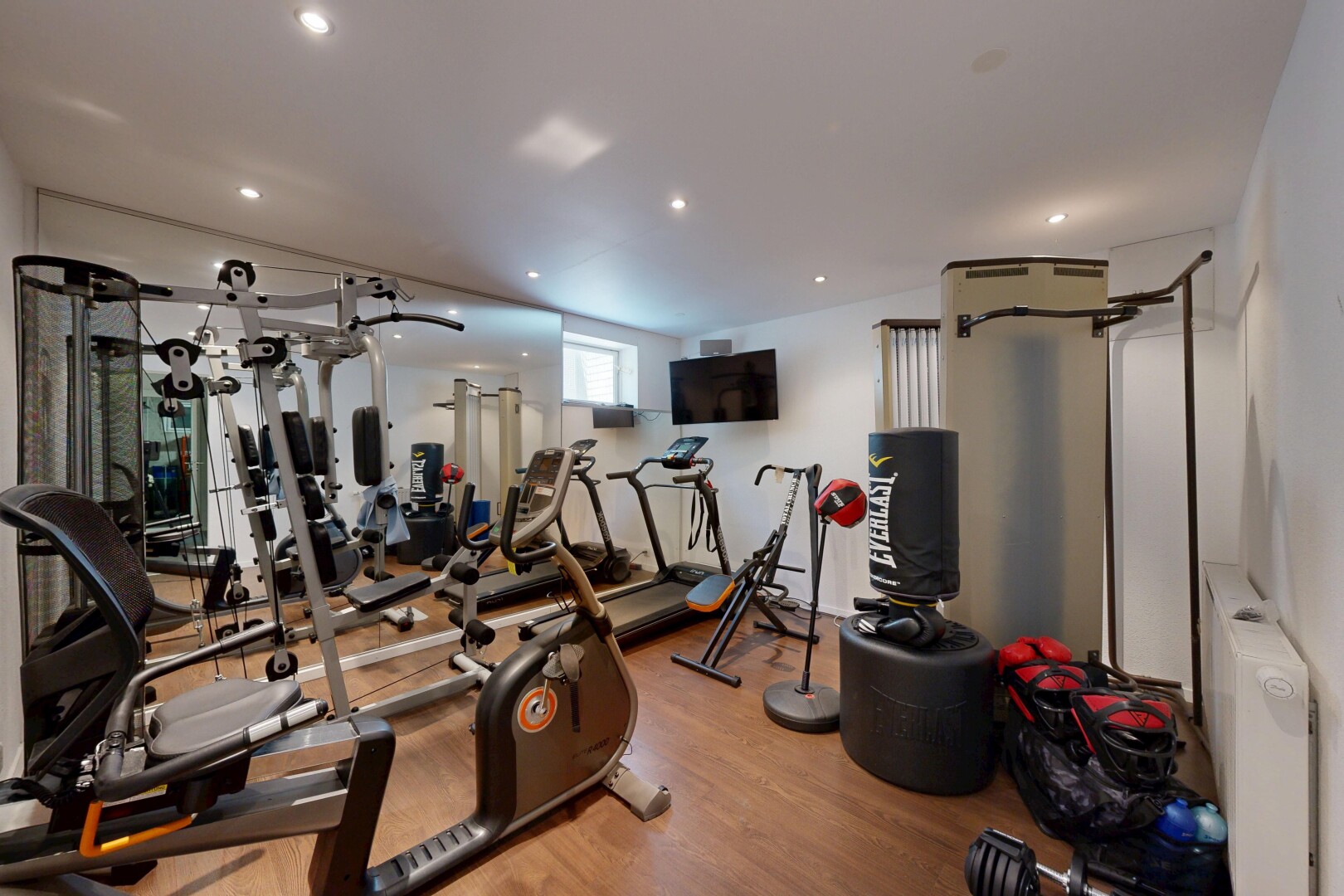 gym avec inside property, radiateur, wood finish floor, sol en finition bois, et télévision