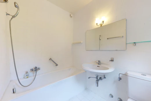 salle de bain avec mur carrelé, toilettes, miroir, et bain-douche