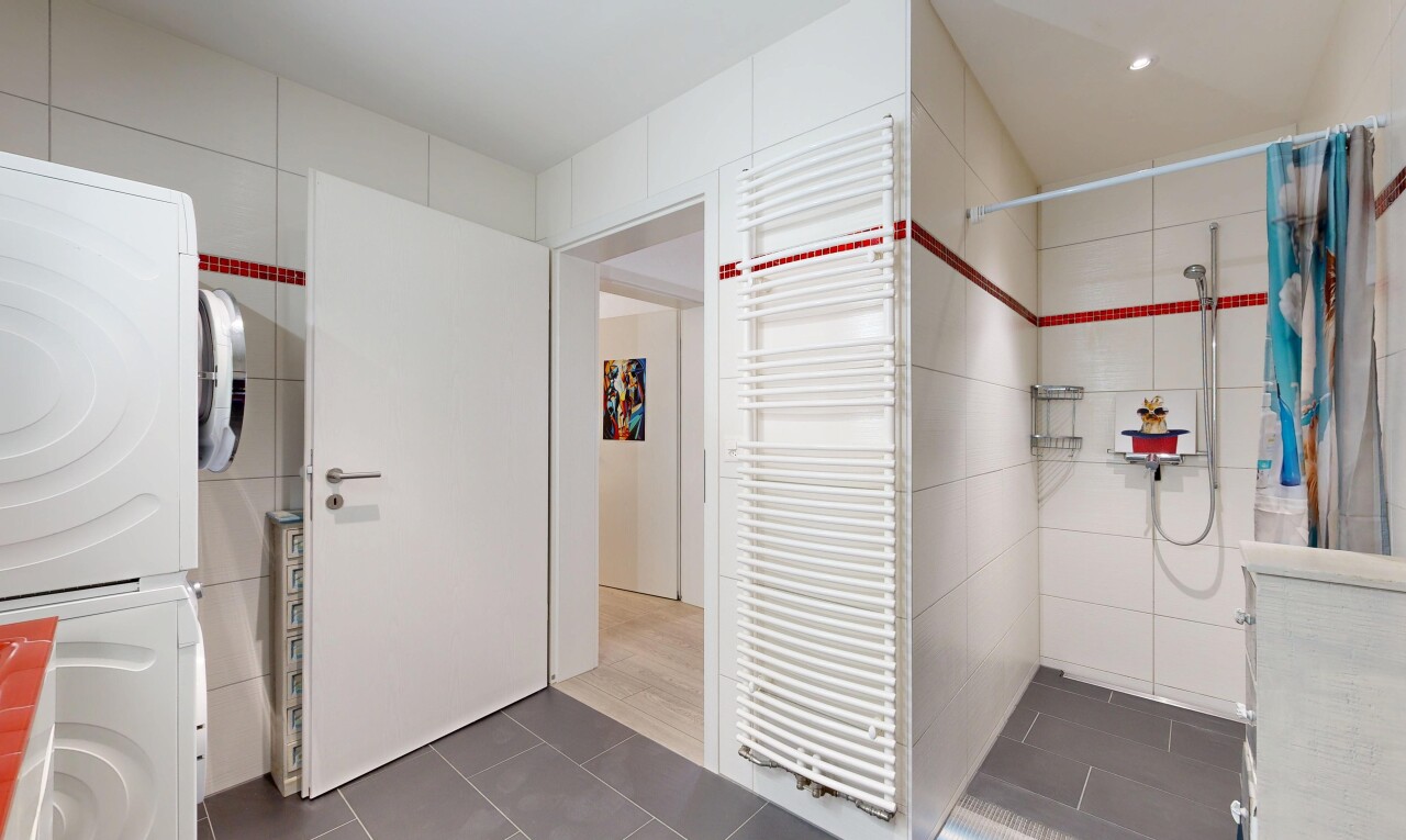full bathroom featuring radiator, dark tile patterned floors, tile walls, tiled shower, and stacked washer and clothes dryer